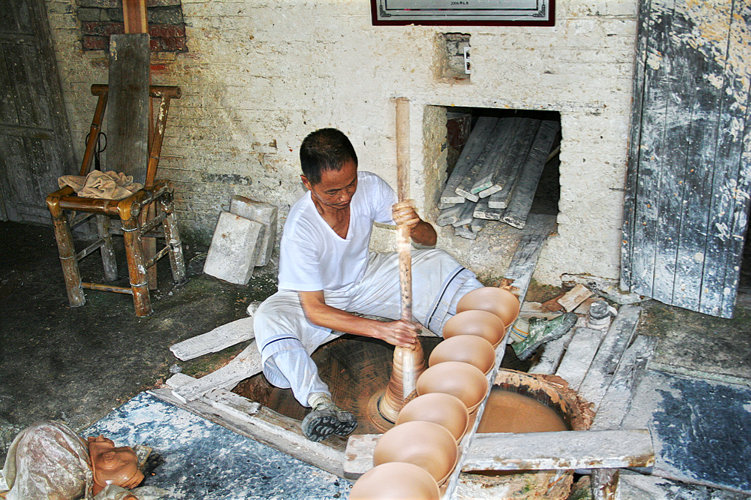 Meister Wang Yansheng bei Drehen an einer in den Boden eingelassenen, von Hand angetriebenen Töpferscheibe im Guyao Museum Jingdezhen.