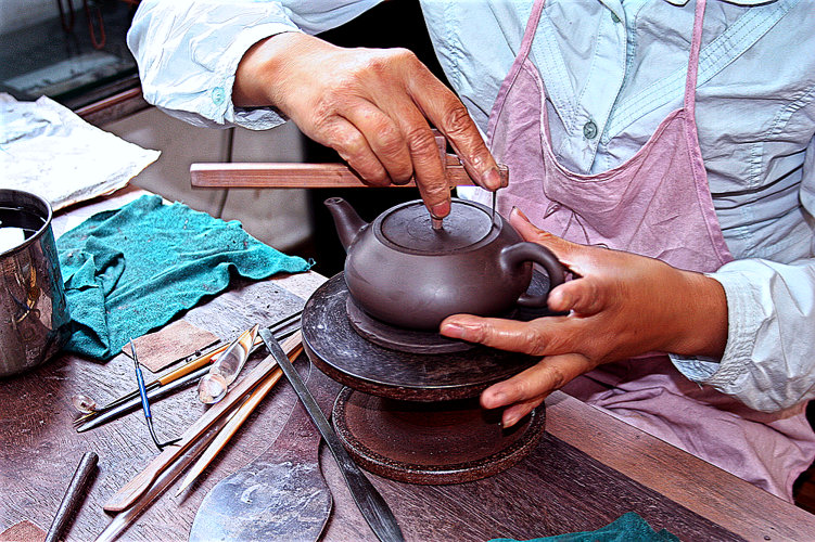 Teekännchenfertigung in Dingshan: Herstellung der Deckel. Nahaufnahme zweier geschickter Hände beim Abmessen und Einpassen der Kännchendeckel.