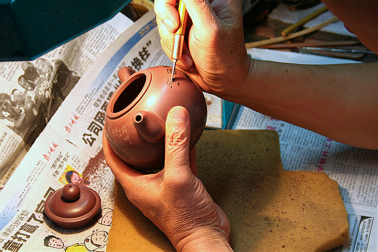 Teekännchenherstellung in Dingshan: Nahaufnahme eines Arbeiters bei der Gravur von Schriftzeichen in ein Teekännchen. Jedes Stück wird individuell von Hand gefertigt, es kann also nach Wunsch graviert werden.