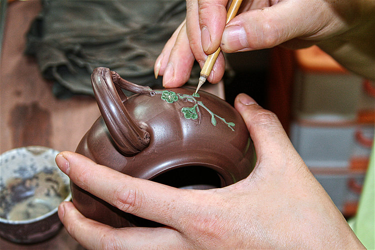 Teekännchenherstellung in Dingshan: Mit feinsten Werkzeugen wird ein grünes Blumendekor auf ein dunkelbraunes Kännchen aufgetragen.